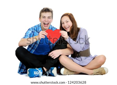 Smiling teenage girl and boy holding a valentine cut out from red paper with scissors over white background