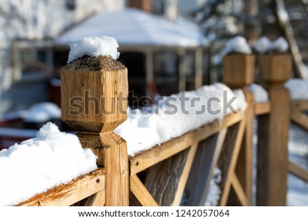 Closeup of wooden deck fence railing side, pole, post covered, in piled, pile of snow after heavy snowing snowstorm, storm at house, home, residential neighborhood in background, trees, sunlight