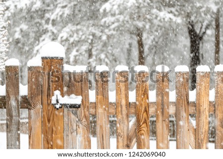 Closeup of wooden fence gate with lock, locked latch covered in white snow at heavy snowing snowstorm, storm, falling snowflakes by house, home with forest in background