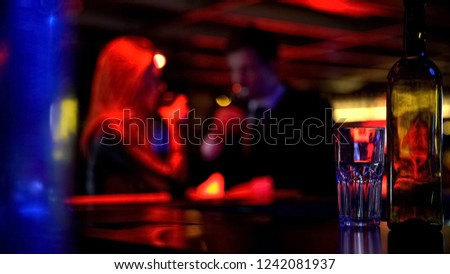 Man and woman dating in nightclub, both drinking beverages, blurred background