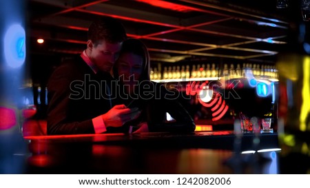 Young happy couple watching pictures on phone in bar, having fun together