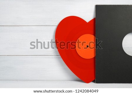 Red vinyl record for a turntable a heart shaped player with a grey cover on a white wooden background of their boards. Listening to Christmas songs. Valentine's Day, Christmas. Ready picture for your