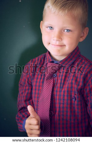 Portrait of smiling preschool boy showing thumb up while standing by the green blackboard.