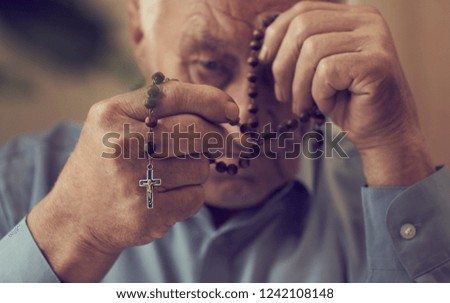 Praying hands of an old man holding rosary beads.