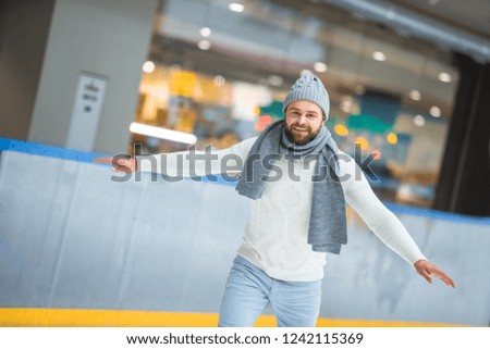 portrait of bearded man in knitted hat and sweater skating on ice rink