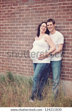 Maternity photos of a couple with brink wall as a background - 8 months pregnant