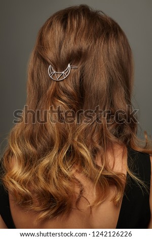 Close up isolated portrait of a lady with wavy ombre hair. The back view of the girl with half-up hairstyle, adorned with openwork silver crescent moon barrette. Posing over the grey background.