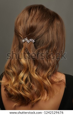 Close up isolated portrait of a young lady with wavy ombre hair. The back view of the girl with half-up half-down hairstyle, adorned with silver floral barrette. Posing against the grey background. Royalty-Free Stock Photo #1242129676
