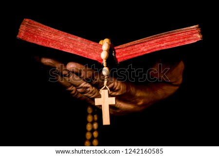 Destroyed hand holding an open book with a rosary, isolated on a black background