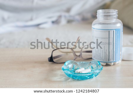Sleeping pills, hypnotic drugs, sedative, melatonin. Capsules in glass bowl with glasses and bottle of pills in table near bed Royalty-Free Stock Photo #1242184807