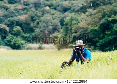 African man travelers take photo and smile happily among green meadows.