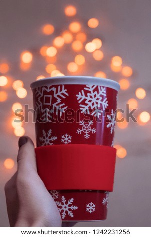 Christmas red cup with snowflakes. Christmas concept. Fairy lights in blurred background