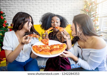Three happy Asian women sharing pizza together for enjoying in front of the Christmas tree on Christmas dinner.
