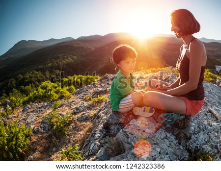 A woman is traveling with a child. Mother with a son is sitting on a large rock. Climb to the top of the mountain with children. The boy with the backpack climbed to the top. Active vacations.