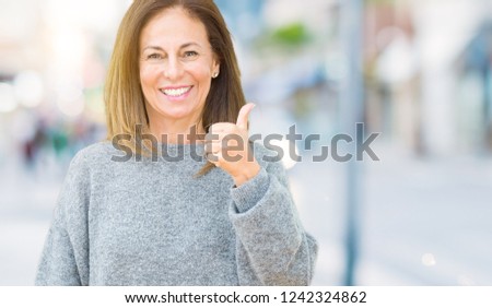 Beautiful middle age woman wearing winter sweater over isolated background doing happy thumbs up gesture with hand. Approving expression looking at the camera showing success.