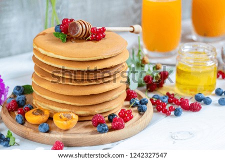 Fresh delicious pancakes with summer raspberries, blueberries, red currants, apricot, peach and mint. Two glasses of orange juice, honey, light background. Sweet nutritious food.