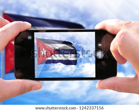 The hands of men make a phone photograph of the flag of Cuba.