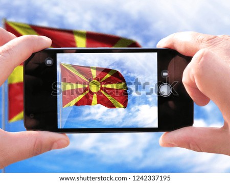 The hands of men make a phone photograph of the flag of Macedonia.