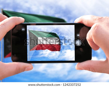 The hands of men make a phone photograph of the flag of Kuwait.