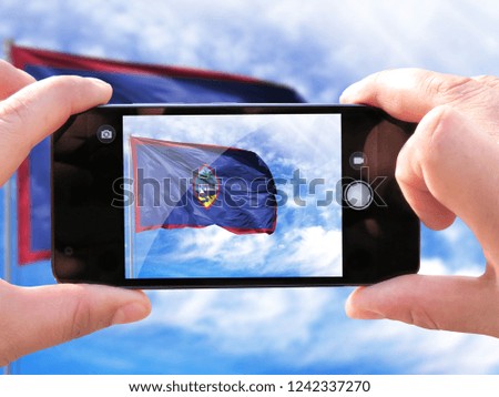 The hands of men make a phone photograph of the flag of Guam.