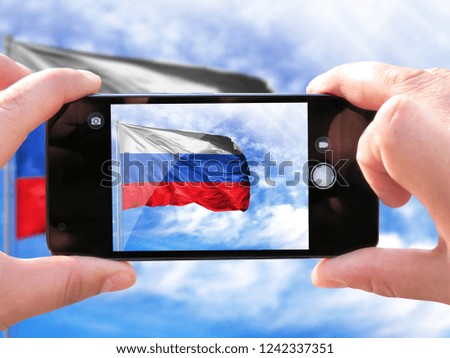 The hands of men make a phone photograph of the flag of Russia.