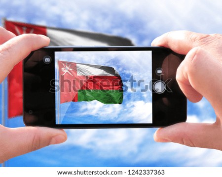 The hands of men make a phone photograph of the flag of Oman.