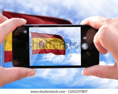 The hands of men make a phone photograph of the flag of Spain.