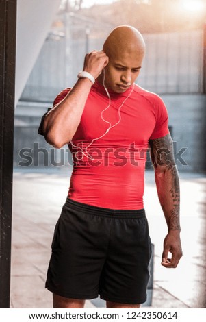 Almost ready. Serious young man looking at his feet while putting on headphones