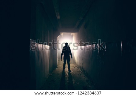 Silhouette of maniac with knife in hand in long dark creepy corridor, horror psycho maniac or serial killer concept, toned Royalty-Free Stock Photo #1242384607