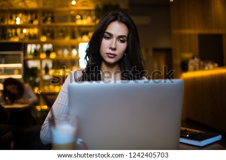 Charming woman skilled freelancer fashion magazine editor typing on laptop computer while sitting in restaurant during recreation time. Pretty female blogger reading article on netbook device 