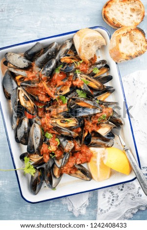 Traditional barbecue Italian blue mussel with baguette and tomatoes in white wine as top view on a tray 