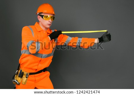 Serious builder measurer with meter roulette in the hands isolated on gray background.