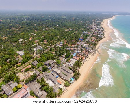 Beach and palm trees with coconuts on beach in Hikkaduwa, Sri Lanka.  Aerial view of town of Hikkaduwa with its beaches, surfspots and buildings. Beautiful tropical beach with great waves for surfing.