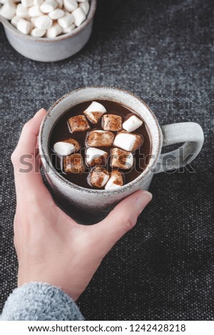A woman reaches for a cup of hot carob (naturally caffeine free) topped with marshmallows.