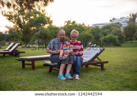 portrait of young happy family with a little daughter  sitting on the sunbed in the beautiful tropical park