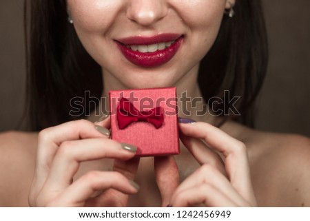 The portrait of the woman with red lipstick isolated on the dark gray brown background cropped smiling with giftbox in the hands