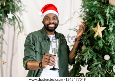Afro american guy with charming smile holding champagne near Christmas tree