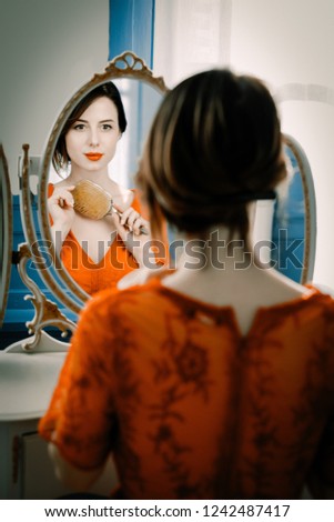 portrait of beautiful young woman with comb looking at herself in the wonderful mirror and sitting next to it