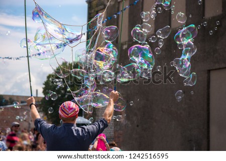 A freelance clown blowing hundreds of tiny, small and big bubbles at outdoor festival in city center. Concept of entertainment, birthdays. Kids having fun. Shower of bubbles flying in the happy crowd

