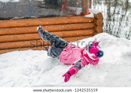 Cute little girl in pink sport suit having fun playing outdoors during snowfall in winter. Children winter seasonal outdoor activities