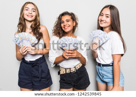 Portrait of multiethnic women expressing irritation while lucky female friend holding lots of money dollar cash over gray background
