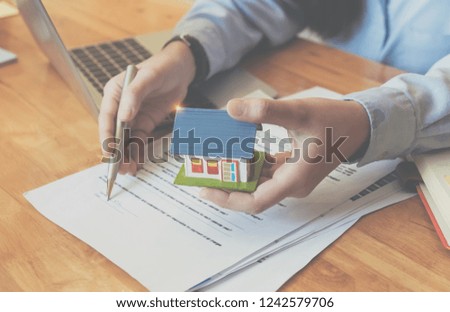 Cropped image of real estate agent assisting client to sign contract paper at desk with house model