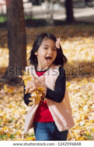 blurred picture of happy little girl carry yellow leaves, filtered tones