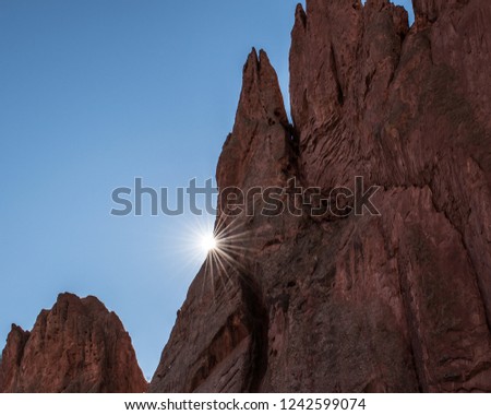 The sun peeking out from behind a jagged rock formation and creating a sunburst in Garden of the Gods, Colorado.