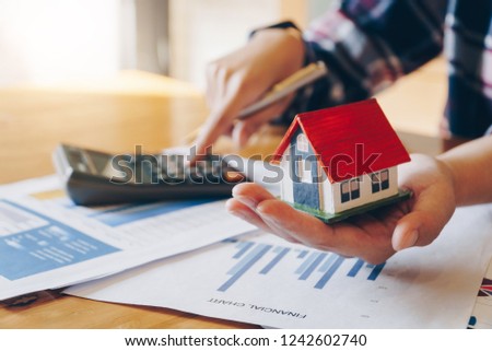 Woman holding house model in hand and calculating financial chart for investment to buying property. Royalty-Free Stock Photo #1242602740