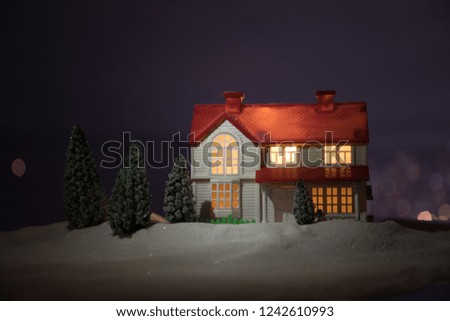 Christmas and New Year miniature house in the snow at night with fir tree. Little toy house on snow with tree and bokeh city lights on background. Christmas decorations. Holiday concept.
