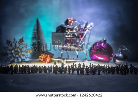 New year or Christmas holiday shopping concept. Store promotions. Silhouette of a large crowd of people watching at a big shopping trolley with gifts. People on snow ready to shopping. Selective focus