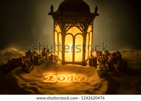 Christmas lantern on snow with gifts at night. Festive dark background. New Year's still-life postcard. Lamp covered in snow with glowing candle at night. Holiday concept. Artwork