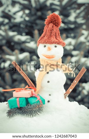 Vintage photo, Snowman in woolen scarf and cap with gift for Christmas, background of coniferous tree covered snow