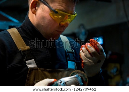A man sharpens a drill with a grinding machine with gloves and yellow glasses.
